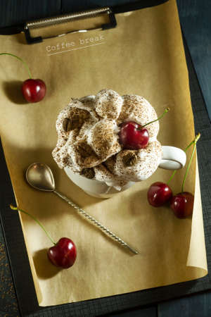 Chocolate cake with cherries and a cup of coffee with whipped cream. Coffee break. Wooden dark blue backgroundの写真素材