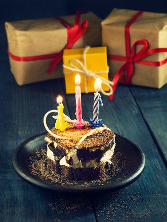 Chocolate cake with a candle and gifts.Happy Birthday, card. Holidays greeting card. Wooden dark blue backgroundの写真素材