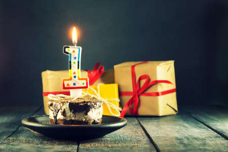 Chocolate cake with a candle and gifts.Happy Birthday, card. Holidays greeting card. Wooden dark blue backgroundの写真素材