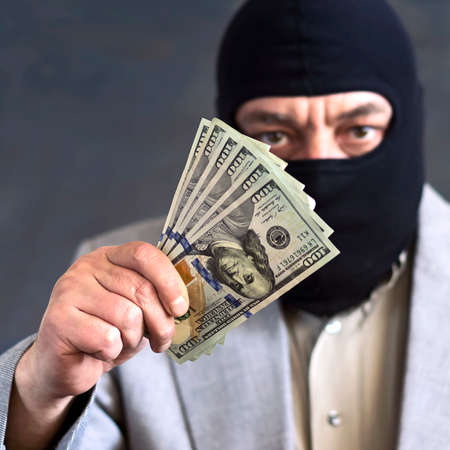 Businessman in balaclava with dololors in hands on dark background. Crime. Theft. Not an honest businessの写真素材