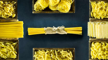 Different kind of Italian pasta in wooden boxes on a dark blue background