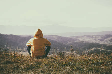 The girl in the hood looks at the beautiful mountains. Solitude with nature. Tourism. Travels. Tinted photo. Mountain landscape.の写真素材