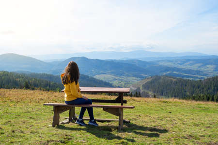 Girl sits on a wooden bench and admires the beautiful mountain landscape. Recreation. Travels. Tourism.の写真素材