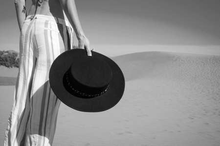 Woman holding a hat in her hand on the background of sand dunes and blue sky. Black and white...