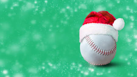 Baseball ball in Santa hat, on a green background. Copy space. Snow effect. Festive background