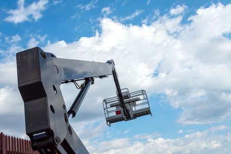 Hydraulic lifting platform with a bucket on a blue, cloudy sky. Building. Industry. Construction machinery. Background.の写真素材
