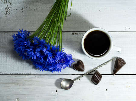 Blue wildflowers with a cup of coffee and candies on a white wooden table