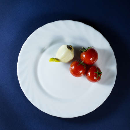 Tomatoes and clove of garlic in white plate on a dark blue backgroundの写真素材