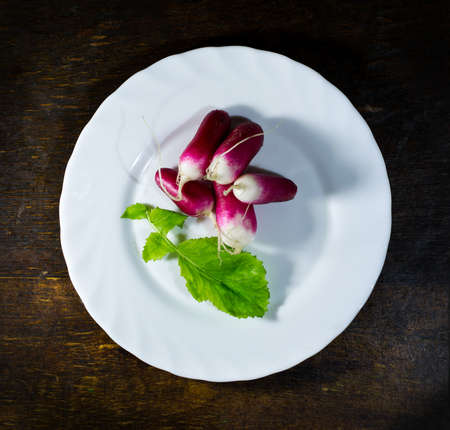 Fresh radishes in white plate on old wooden tableの写真素材