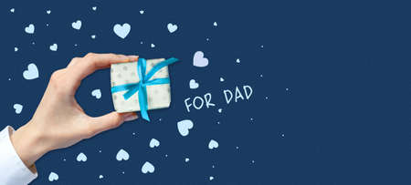 Female hand with a gift on a dark background. Copy space. Place for text. Father's Day. Greeting...