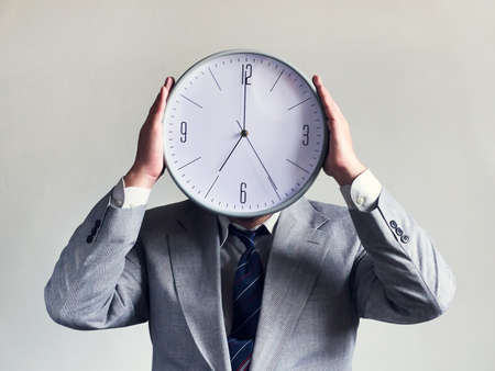 Businessman with a clock instead of a head. Concept business and efficiency. Time and schedule. Money and time. Gray backgroundの写真素材