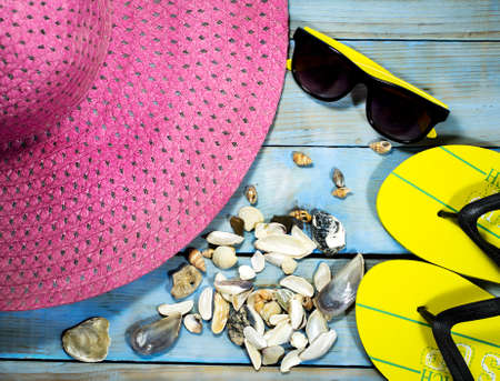 Fashion accessories summer flip flops, hat, sunglasses and seashells on a blue wooden background....