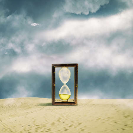 Hourglass in the sand dunes. Cloudy sky. Time concept. Business. Lifestyle. Square orientation. Abstraction background.の写真素材