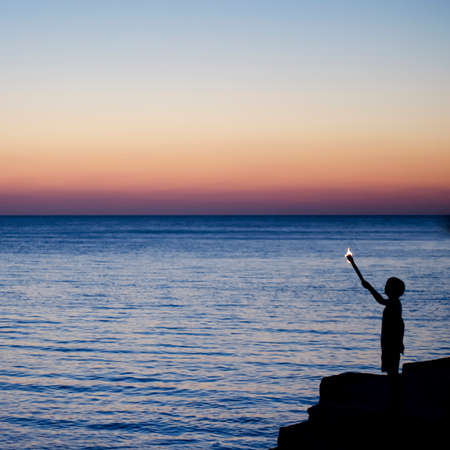 Silhouette of a boy with a torch at sunset over the ocean. Freedom. Travels. Square orientation.の写真素材