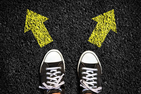 Sneakers on an asphalt road. Yellow arrows pointing in different directions. View from above. The concept of choosing the right path. Business. Lifestyle. Background.の写真素材
