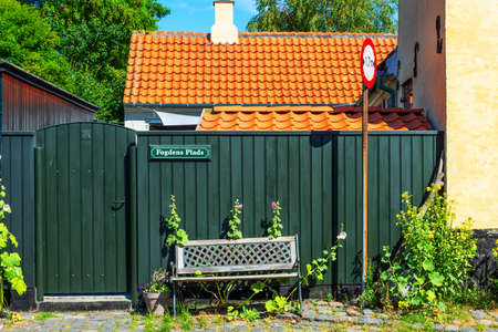 Dragor. Denmark. July 24, 2019. A beautiful bench, and an entrance gate, in front of a rustic yellow house. Traditional Scandinavian style. Fishing village. Sights. Travels.のeditorial素材