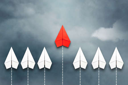 Red paper plane flying in front of a group of whites. Cloudy sky. Leadership concept, teamwork, personnel management. Business. Lifestyle. Background.の写真素材