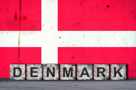 Denmark, words on stone blocks, on grunge background of Denmark flag, on a concrete wall. copyspace. Signs and symbols.Countries.の写真素材