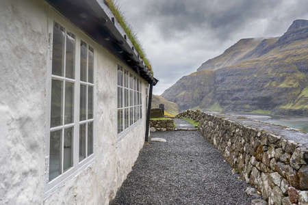 Beautiful little church, with a grassy roof, against the backdrop of beautiful mountains, and dramatic clouds. Faroe Islands. Denmark. Europe. Landscapes. Nature.の写真素材