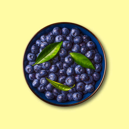 Blueberries with green leaves in a bowl, isolated on a yellow background. Healthy food. Diet. Top view. Berries.の写真素材