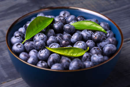 Blueberries with green leaves in a bowl, on a dark blue wooden background. Close-Up. Healthy food. Diet. Top view. Berries.の写真素材