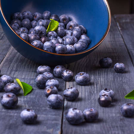 Blueberries with green leaves in a bowl, scattered on a wooden table. Close-up. Selective focus. Healthy food. Diet. Top view. Berries.の写真素材