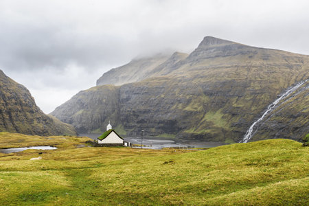 Beautiful little church, with a grassy roof, against the backdrop of beautiful mountains, and dramatic clouds. Faroe Islands. Denmark. Europe. Landscapes. Nature.の写真素材