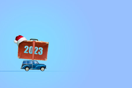 Car with a suitcase on the roof. 2023, number. Santa Claus hat. On a blue background. copy space. New Year card. Festive background.の写真素材