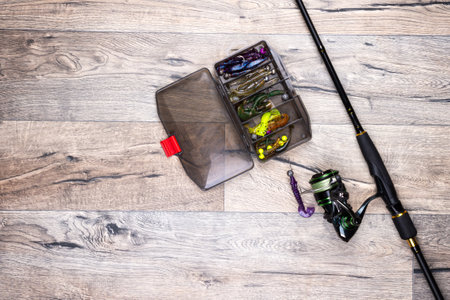 Spinning rod with a reel and a box of baits on a gray wooden background. Copy space. Fishing...