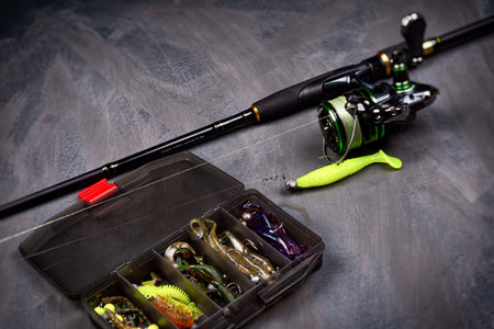 Spinning rod with a reel and a box of baits on a dark background. Copy space. Fishing background.の写真素材