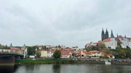 A beautiful town is seen along the river, featuring colorful buildings and historic architecture. Overcast skies create a soft light as trees hint at autumn colors.の写真素材