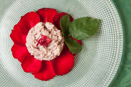 Carnaroli rice rose risotto decorated with red rose petals and leaves, close up, on glass plate and green tableclothの写真素材