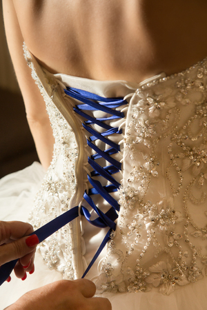 white strapless beaded bridal gown with blue corset lacing being laced, rear viewの写真素材