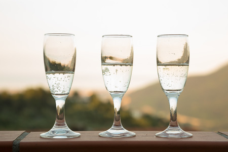 Three glasses full of sparkling wine against the mountains at sunsetの写真素材