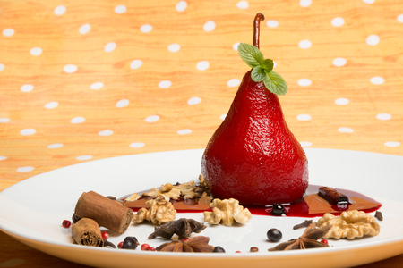 White dish with pear flavored with red wine, Brachetto syrup and crunch nuts, cinnamon, star-anise, red pepper, juniper berries and a mint leafの写真素材