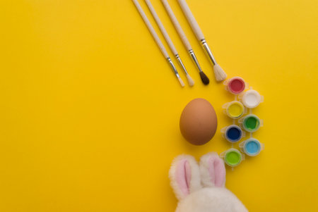 Easter bunny with easter eggs and paintbrushes on yellow backgroundの写真素材