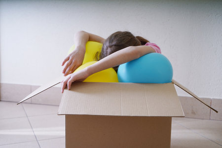 Little girl playing with a ball on the floor in a cardboard boxの写真素材