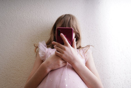 Girl in a pink dress with a phone in her hands on a white backgroundの写真素材