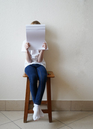 Girl sitting on a chair and holding a sheet of paper in her handsの写真素材