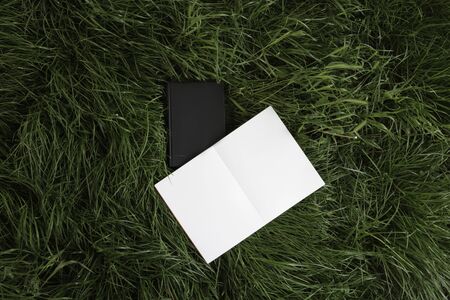 Black book and notebook lie on the grass, background. Layout notebook and book. White notebook with...