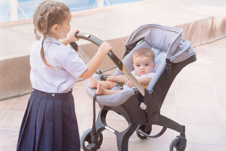Children are walking. An older girl is walking with a baby. Sister take care