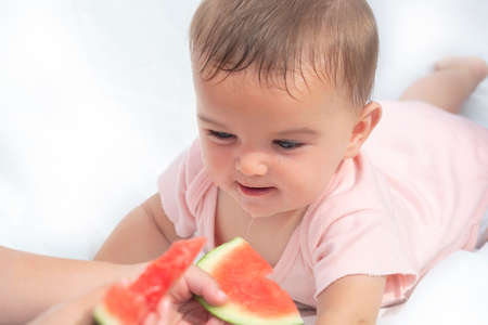 interested cute baby looks at the red juicy watermelon. drooling from the chin. the child wants to...