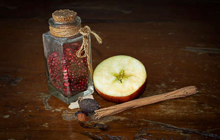 ingredients and spices. pink pepper in a jar, half an apple, cinnamon sticks. on a wooden background. preparation for the holidays.の写真素材