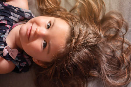 high angle portrait of pretty young girl, with beauty long hair, lying on gray background. Hair care...
