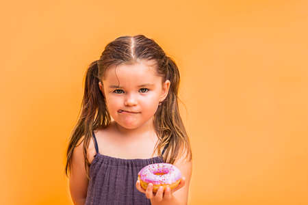 cute child holds donut in hands and licks his lips.の写真素材