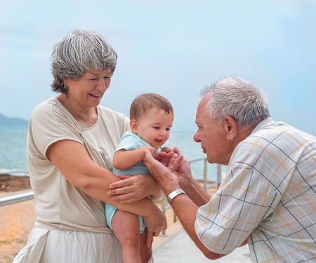 happy family on a walk. Grandmother holds the baby, great grandfather plays with the child on the embankment.の写真素材