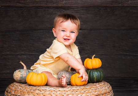 cut baby girl playing with small pumpkin sitting on the rattan chair on dark wooden backgraundの写真素材