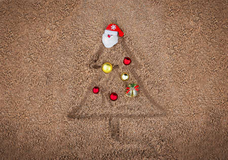 painted christmas tree on the sand on the beach with christmas ornament toy santa clausの写真素材