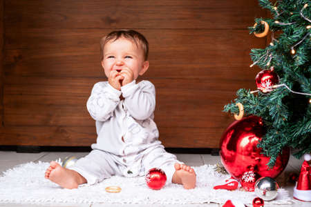 Cute baby on the floor at home and eating a bagel. Celebrating Christmas near the Christmas treeの写真素材