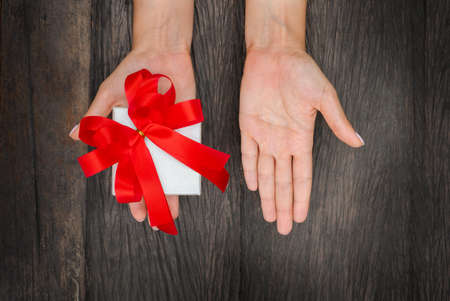 gift box with a red bow in hand on a wooden background. hand free for copy space